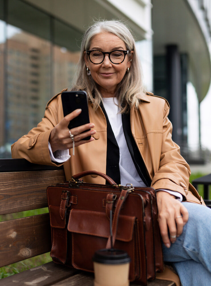 beautiful mature woman checking her phone on city bench